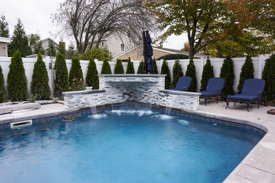 Triple-tiered stacked stone sheer descent waterfalls flowing into a backyard pool with evergreen landscaping