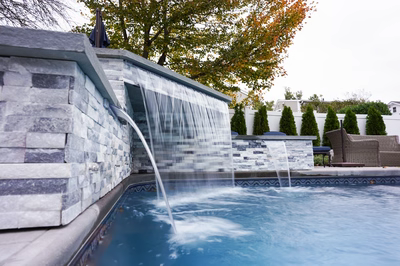 Multi-tiered natural stone boulder waterfalls cascading into a swimming pool with manicured evergreen surroundings