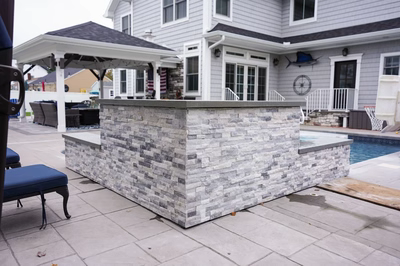 Two-tiered natural stone boulder waterfall cascading into a rectangular pool beside a paved patio