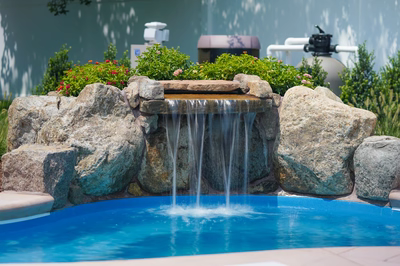Single-tier natural stone boulder waterfall with sheer flow into pool surrounded by lush greenery