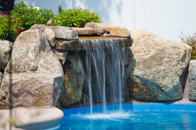 Single-tier natural stone boulder waterfall cascading into a pool with lush green garden plants