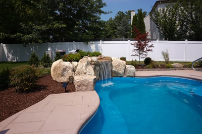 Single-tier natural stone boulder waterfall cascading into a blue pool surrounded by garden plants