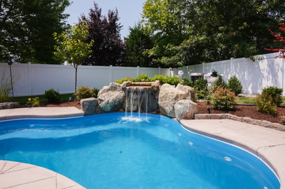 Single-tier natural stone boulder waterfall cascading into a blue pool with surrounding garden plants