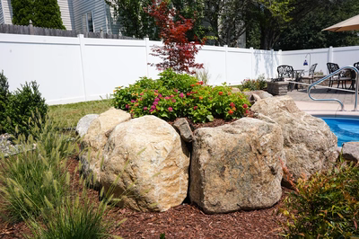 Natural stone boulder waterfall cascading into a swimming pool surrounded by lush garden plants