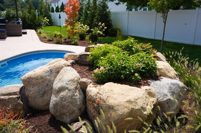 Two-tiered natural stone boulder waterfall cascading into a pool surrounded by vibrant garden landscaping
