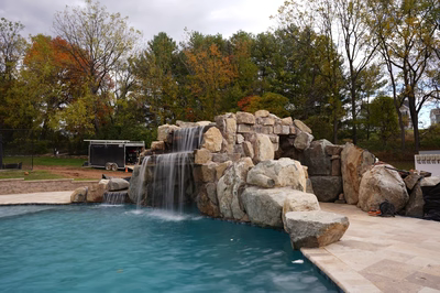 Two-tiered natural stone boulder waterfall cascading into a swimming pool with colorful autumn trees