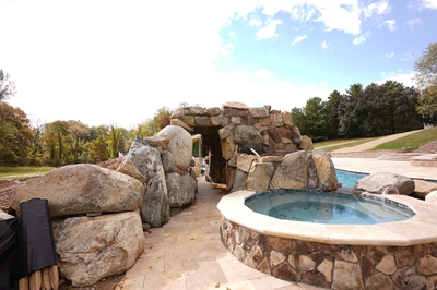 Multi-tiered natural stone boulder waterfall cascading into a pool area surrounded by mature trees