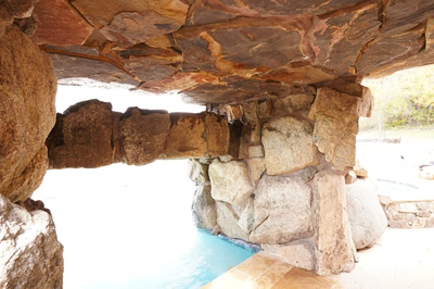 Single-tier natural stone boulder waterfall cascading into a clear pool with lush garden plants