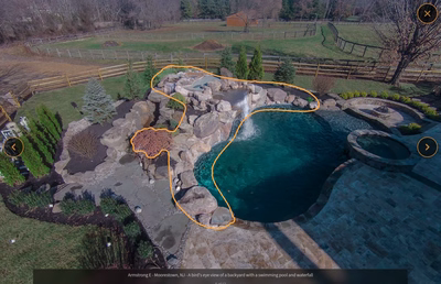Multi-tiered natural stone boulder waterfall cascading into a freeform pool with surrounding evergreen landscaping