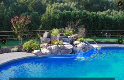 Two-tiered natural stone boulder waterfall cascading into a blue pool surrounded by lush greenery