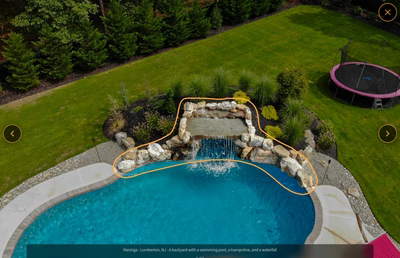 Two-tiered natural stone boulder waterfall cascading into a freeform pool with lush landscaping