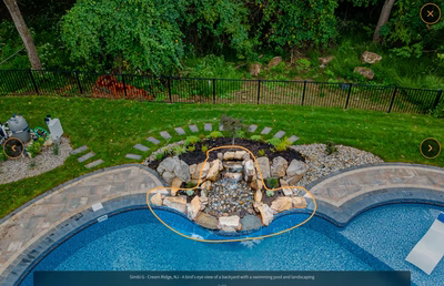 Multi-tiered natural stone boulder waterfall cascading into a pool surrounded by lush backyard landscaping