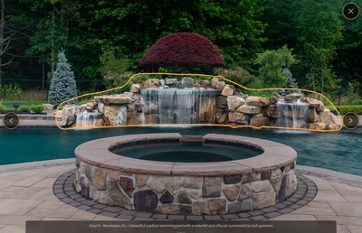 Multi-tiered natural stone boulder waterfall cascading into a swimming pool surrounded by lush greenery
