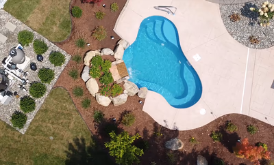 Two-tiered stone boulder waterfall cascading into a freeform pool surrounded by mulch and plants
