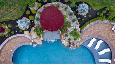 Multi-tiered natural stone boulder waterfall cascading into a pool surrounded by lush, colorful landscaping