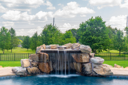 Patterson A - Medford, NJ - A large rock waterfall in the middle of a swimming pool surrounded by lush green grass and trees