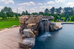 Patterson D - Medford, NJ - A large rock waterfall in the middle of a swimming pool surrounded by lush green grass and trees