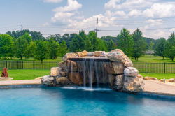 Patterson E - Medford, NJ - A large rock waterfall in the middle of a swimming pool surrounded by lush green grass and trees